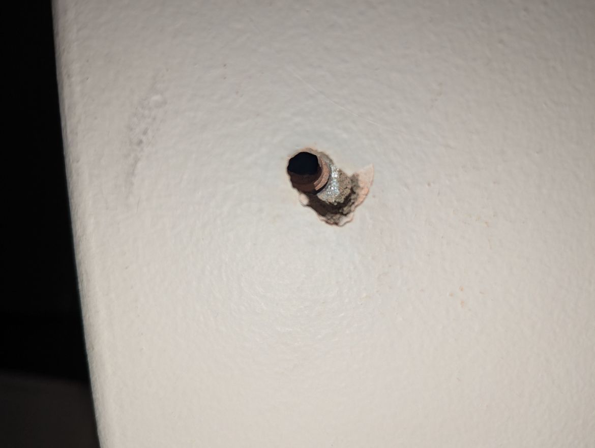 Drill hole with edge of metal plate, between brick and plaster